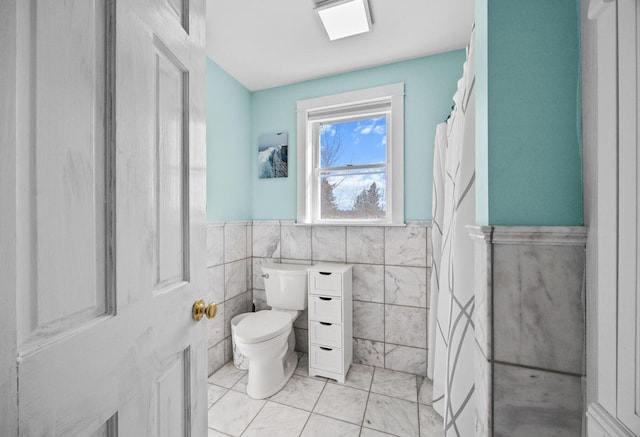 bathroom with toilet, tile walls, and a wainscoted wall