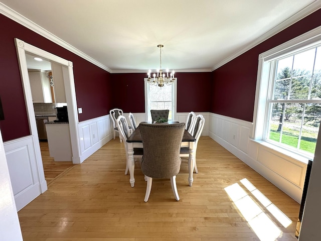 dining space featuring crown molding, a notable chandelier, wainscoting, and light wood finished floors