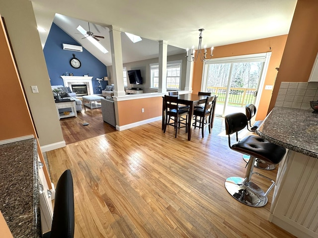 dining room with a glass covered fireplace, a wealth of natural light, ceiling fan with notable chandelier, and light wood-type flooring