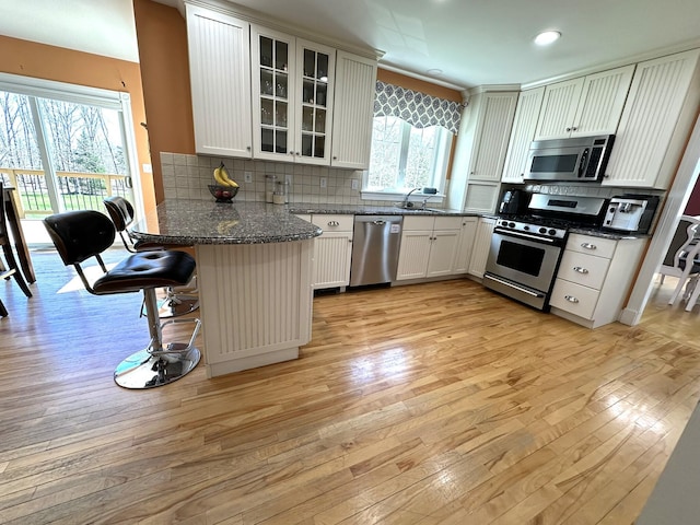 kitchen with a peninsula, appliances with stainless steel finishes, glass insert cabinets, and light wood finished floors