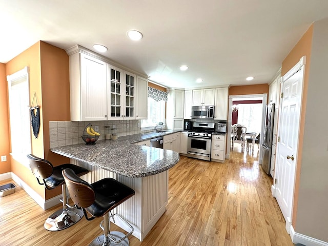 kitchen with light wood-type flooring, a peninsula, a sink, and appliances with stainless steel finishes