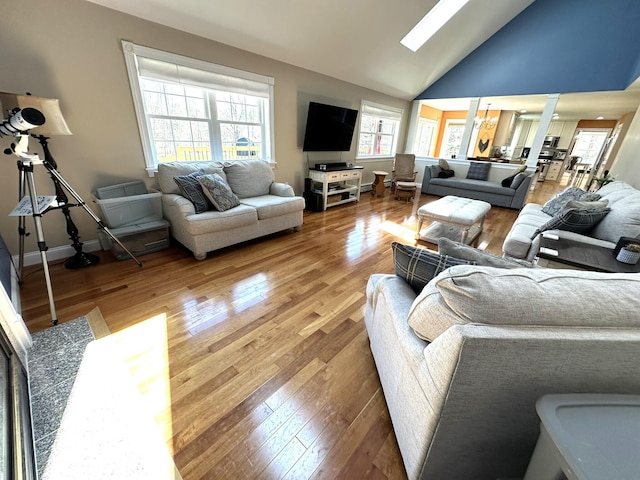 living room featuring light wood-type flooring, decorative columns, baseboards, and vaulted ceiling with skylight