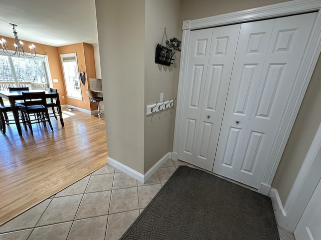 hall with light tile patterned floors, baseboards, and a chandelier