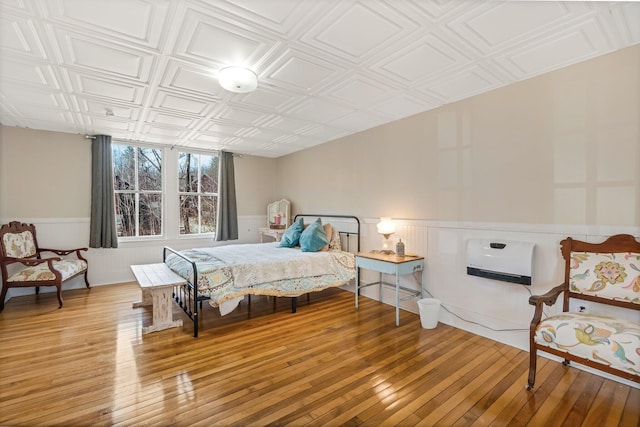 bedroom featuring hardwood / wood-style floors, heating unit, a wainscoted wall, and an ornate ceiling