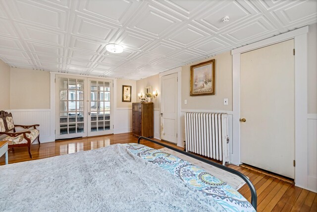 bedroom with wood finished floors, radiator, a wainscoted wall, an ornate ceiling, and french doors