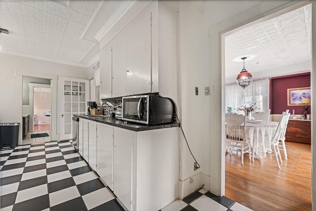 kitchen with light floors, dark countertops, a sink, white cabinetry, and crown molding