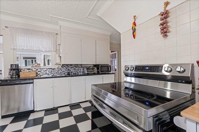 kitchen featuring decorative backsplash, tile patterned floors, stainless steel appliances, white cabinets, and dark countertops