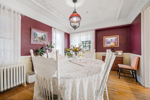 dining area featuring crown molding, a wainscoted wall, wood-type flooring, radiator heating unit, and a notable chandelier