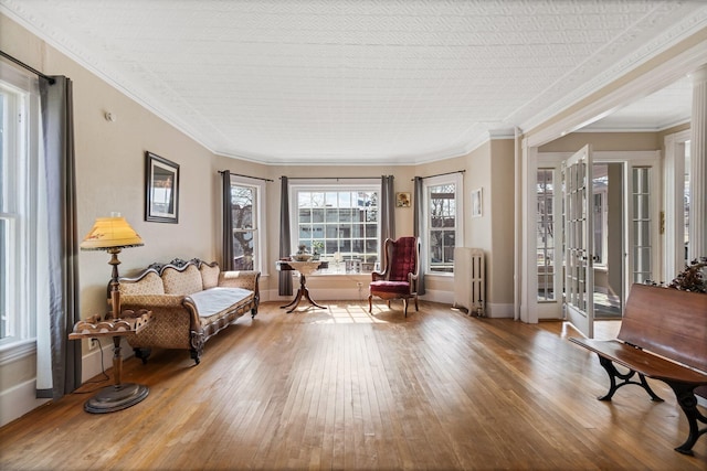 sitting room featuring wood-type flooring, radiator, ornamental molding, and baseboards