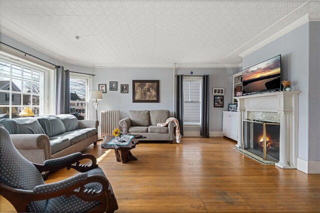 living room featuring ornamental molding, hardwood / wood-style floors, radiator heating unit, and a high end fireplace