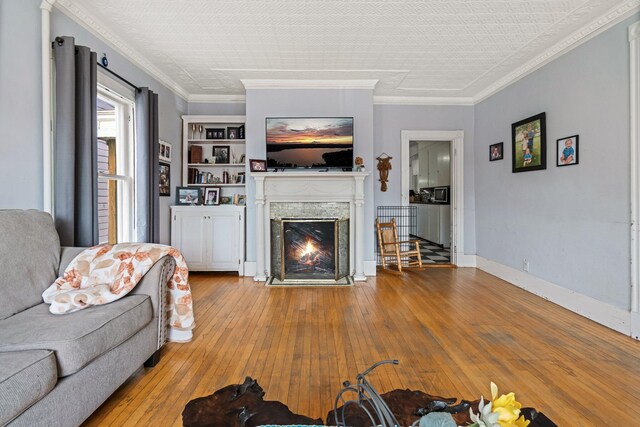 living room featuring wood-type flooring, crown molding, a high end fireplace, and baseboards