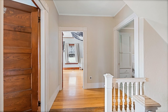 hallway with ornamental molding, an upstairs landing, baseboards, and light wood-type flooring