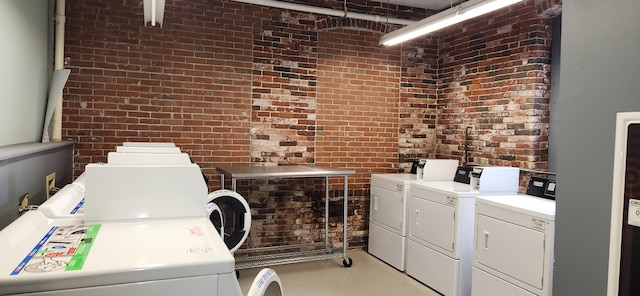 laundry room with washing machine and clothes dryer and brick wall