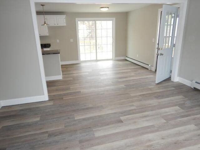 unfurnished dining area featuring light wood-style flooring, a baseboard heating unit, and baseboards