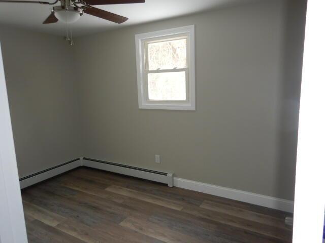 empty room with a baseboard radiator, dark wood-style flooring, ceiling fan, and baseboards