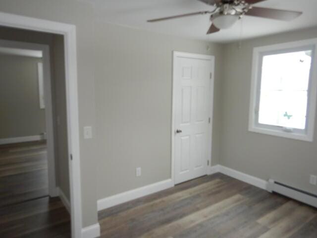 unfurnished bedroom featuring baseboard heating, baseboards, wood finished floors, and a ceiling fan