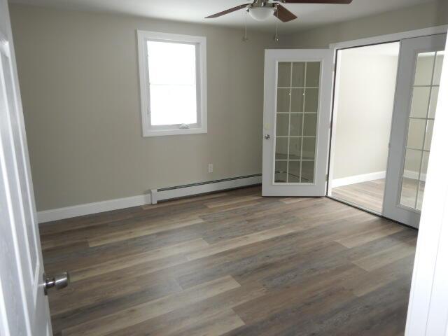 unfurnished room featuring a ceiling fan, baseboard heating, wood finished floors, and baseboards