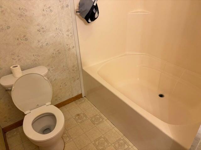 bathroom with baseboards, wallpapered walls, toilet, and a bath