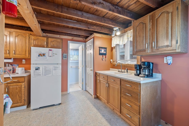 kitchen with freestanding refrigerator, a sink, wood ceiling, light countertops, and beamed ceiling