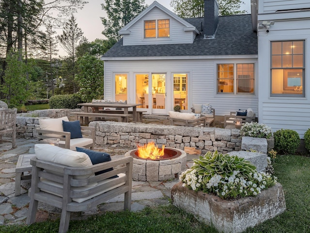 back of house at dusk featuring an outdoor living space with a fire pit, a chimney, a patio area, and roof with shingles