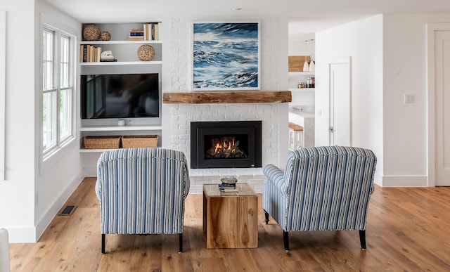 living area with visible vents, baseboards, a brick fireplace, wood finished floors, and built in shelves