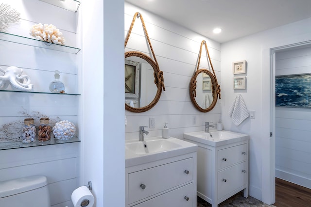 bathroom featuring two vanities, toilet, wood finished floors, and a sink