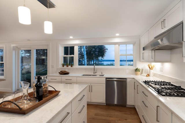 kitchen with a sink, under cabinet range hood, light stone counters, white cabinets, and appliances with stainless steel finishes