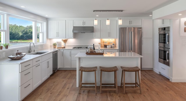 kitchen with a sink, stainless steel appliances, under cabinet range hood, light wood-type flooring, and a center island