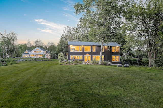 back of property at dusk featuring metal roof, a standing seam roof, a yard, and board and batten siding
