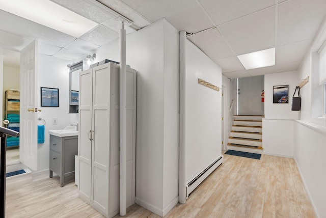 hall with a sink, a baseboard radiator, a drop ceiling, stairs, and light wood-style flooring