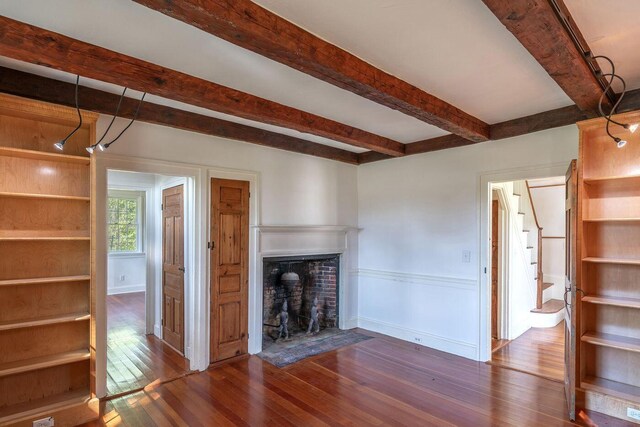 258 River Rd, Eliot, ME 03903 - unfurnished living room with dark wood-style flooring, beam ceiling, a wainscoted wall, stairs, and a fireplace with flush hearth