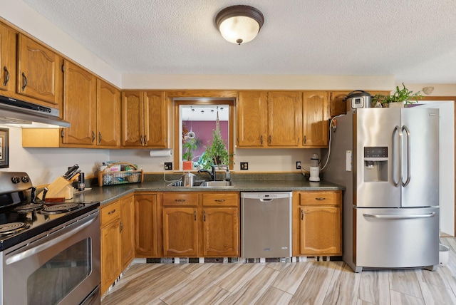 171 Regan Ln, Portland, ME 04103 - kitchen featuring appliances with stainless steel finishes, under cabinet range hood, brown cabinets, a textured ceiling, and dark countertops
