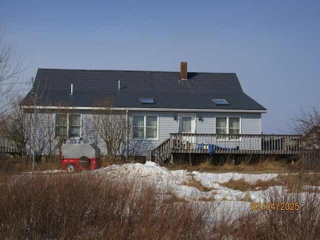 snow covered back of property featuring a chimney, a wooden deck, and roof with shingles
