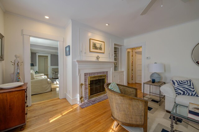 living area with a ceiling fan, crown molding, built in features, a fireplace, and light wood-style flooring