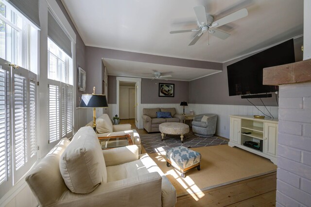 living room featuring crown molding, a ceiling fan, wainscoting, and hardwood / wood-style floors