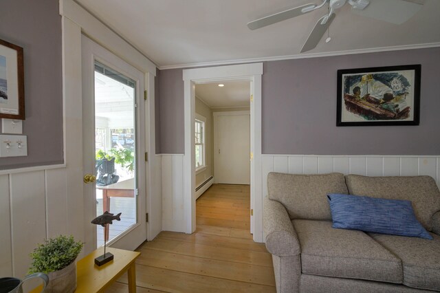 interior space featuring a ceiling fan, crown molding, wainscoting, light wood-type flooring, and a baseboard heating unit