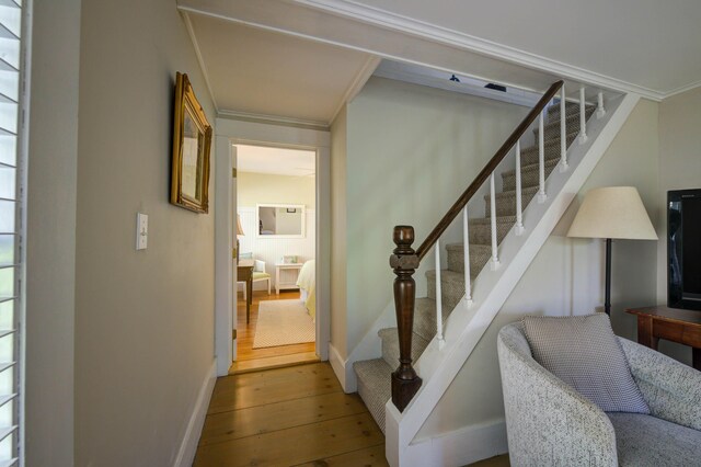 stairs with wood-type flooring, baseboards, and crown molding