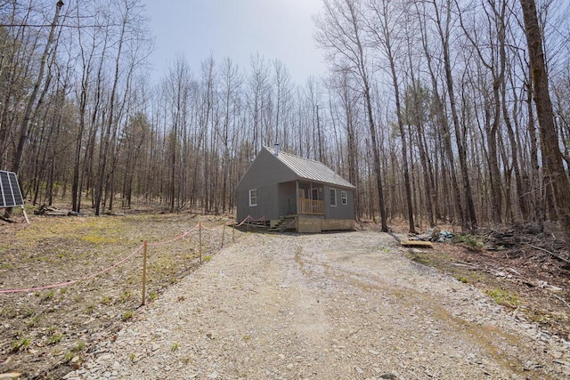 view of property exterior with driveway, metal roof, and a wooded view