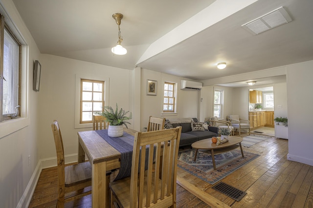 dining room featuring a healthy amount of sunlight, an AC wall unit, light wood-type flooring, and visible vents