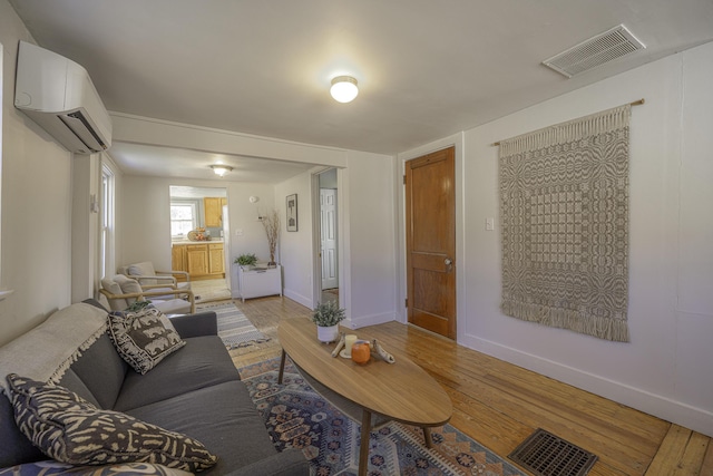 living room with visible vents, light wood finished floors, and a wall unit AC