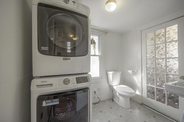bathroom featuring stacked washer and clothes dryer, tile patterned floors, and toilet