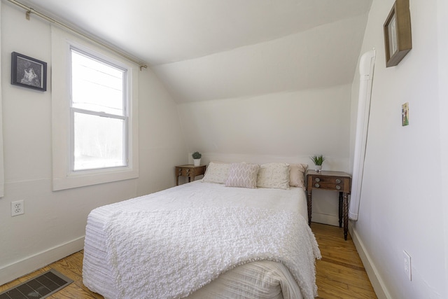 bedroom with baseboards, visible vents, vaulted ceiling, and light wood-style floors