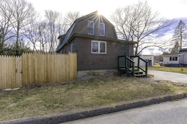 view of side of home featuring fence, a lawn, and a gambrel roof