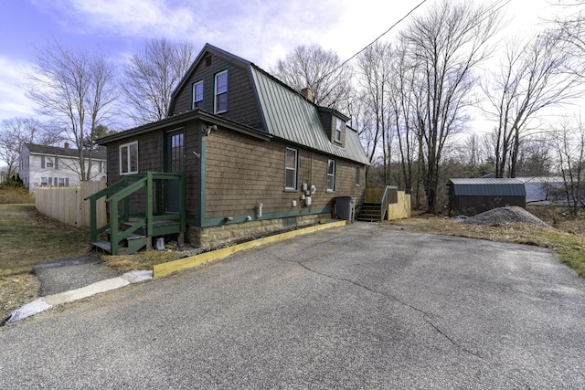 view of side of home featuring a gambrel roof, fence, and metal roof