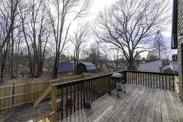 wooden terrace featuring a storage unit, a fenced backyard, and an outbuilding