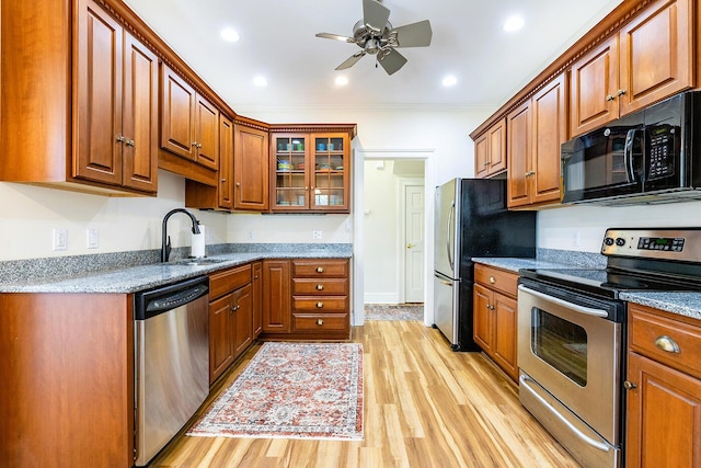 kitchen with brown cabinetry, a sink, a ceiling fan, light wood finished floors, and appliances with stainless steel finishes