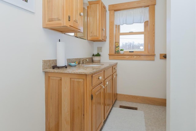 kitchen with a sink, baseboards, light stone countertops, and visible vents