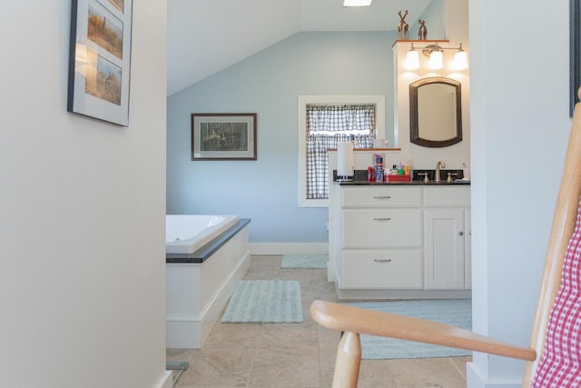 full bath with vanity, baseboards, vaulted ceiling, and a tub