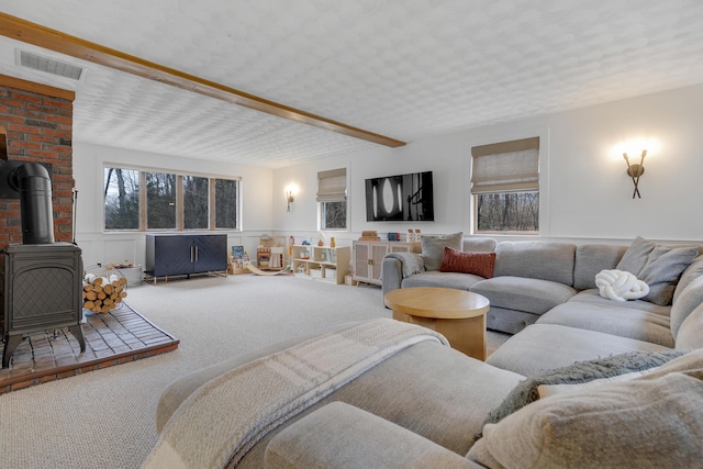 42 Ledge Hill Rd, Raymond, ME 04071 - living room featuring visible vents, a wood stove, beamed ceiling, a wainscoted wall, and carpet