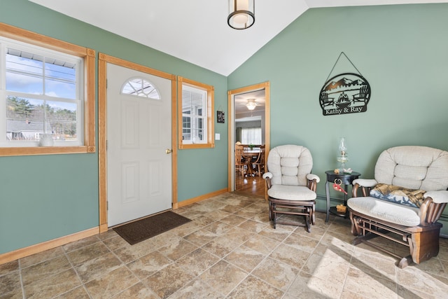 foyer entrance featuring baseboards, stone finish flooring, and high vaulted ceiling